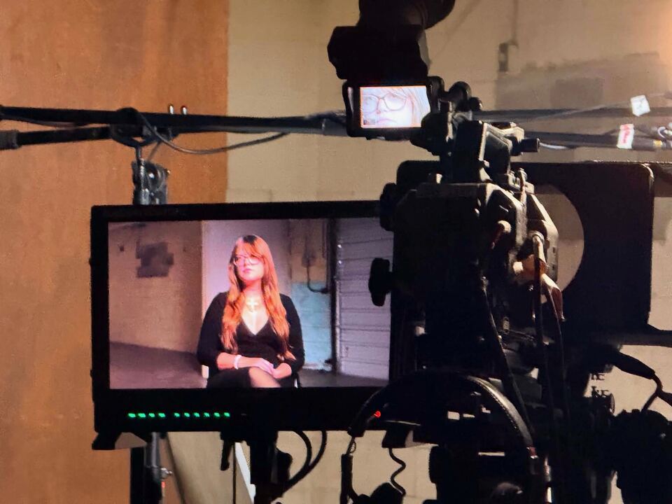 A television camera and monitor on set. Ashlee Willis is
                    visible on the monitor, seated and mid-interview under
                    studio lighting.
