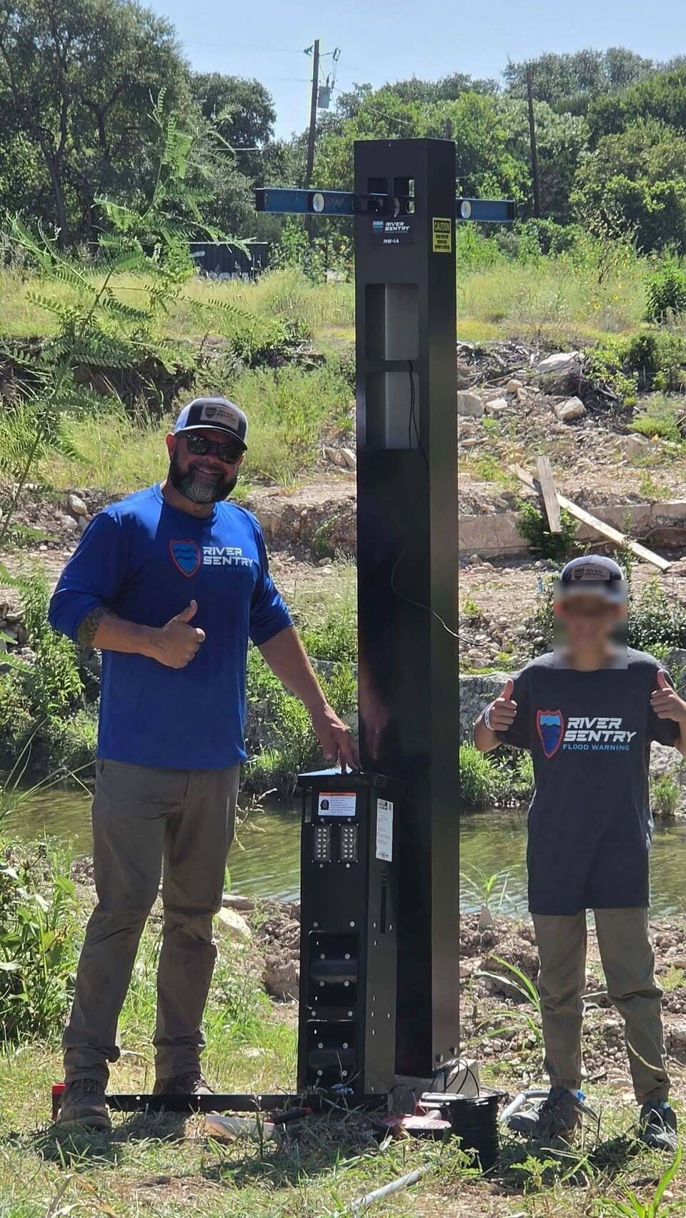 Two people in River Sentry shirts standing either side of the opened device, showing the equipment inside. The younger person's face has been obscured.
