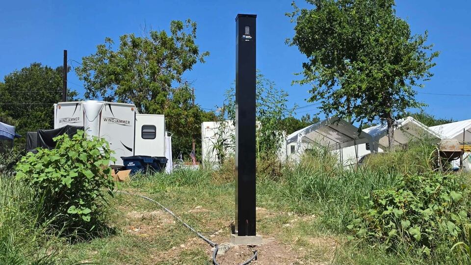 The sensor tower standing in rough grass on the property, with travel trailers parked among the trees behind it.